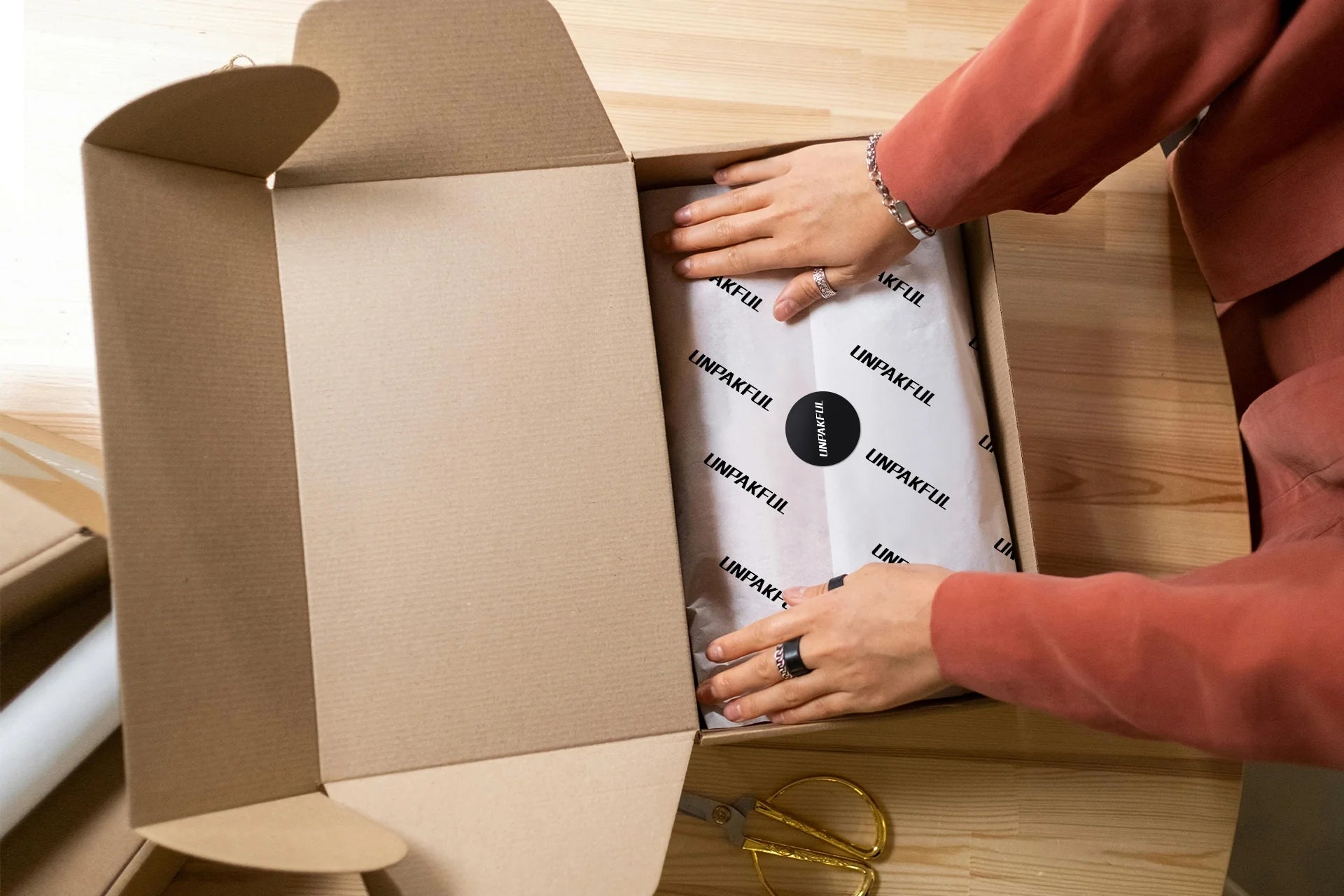 Person placing custom tissue paper inside a kraft box with branding, preparing it for gifting or shipping.