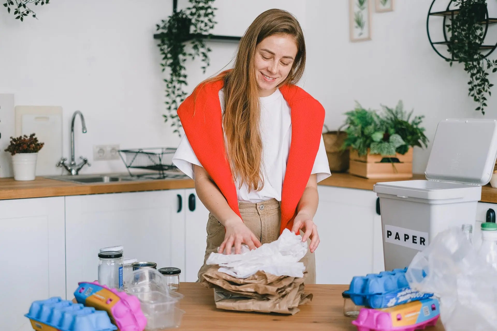 Woman sorting recyclable materials, including tissue paper, in a kitchen with eco-friendly decor.
