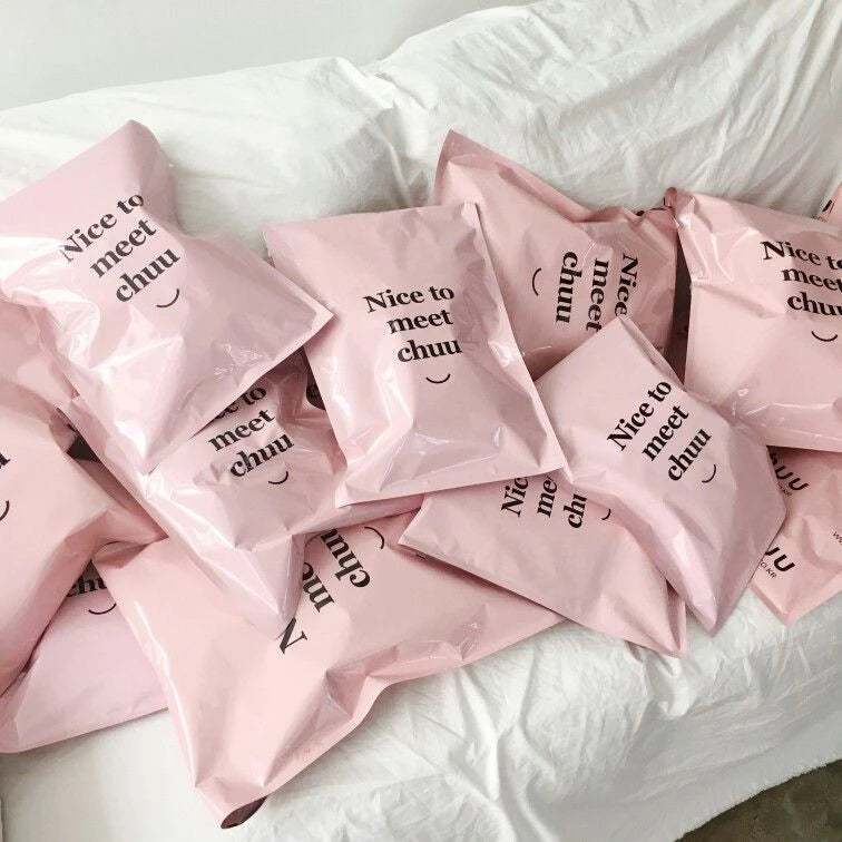 Pile of pink mailer bags with a cheerful message saying "Nice to meet chuu" on them, arranged on a white sofa.