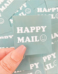 Hand holding a custom square sticker that reads "HAPPY MAIL" with a smiley face on a teal background.