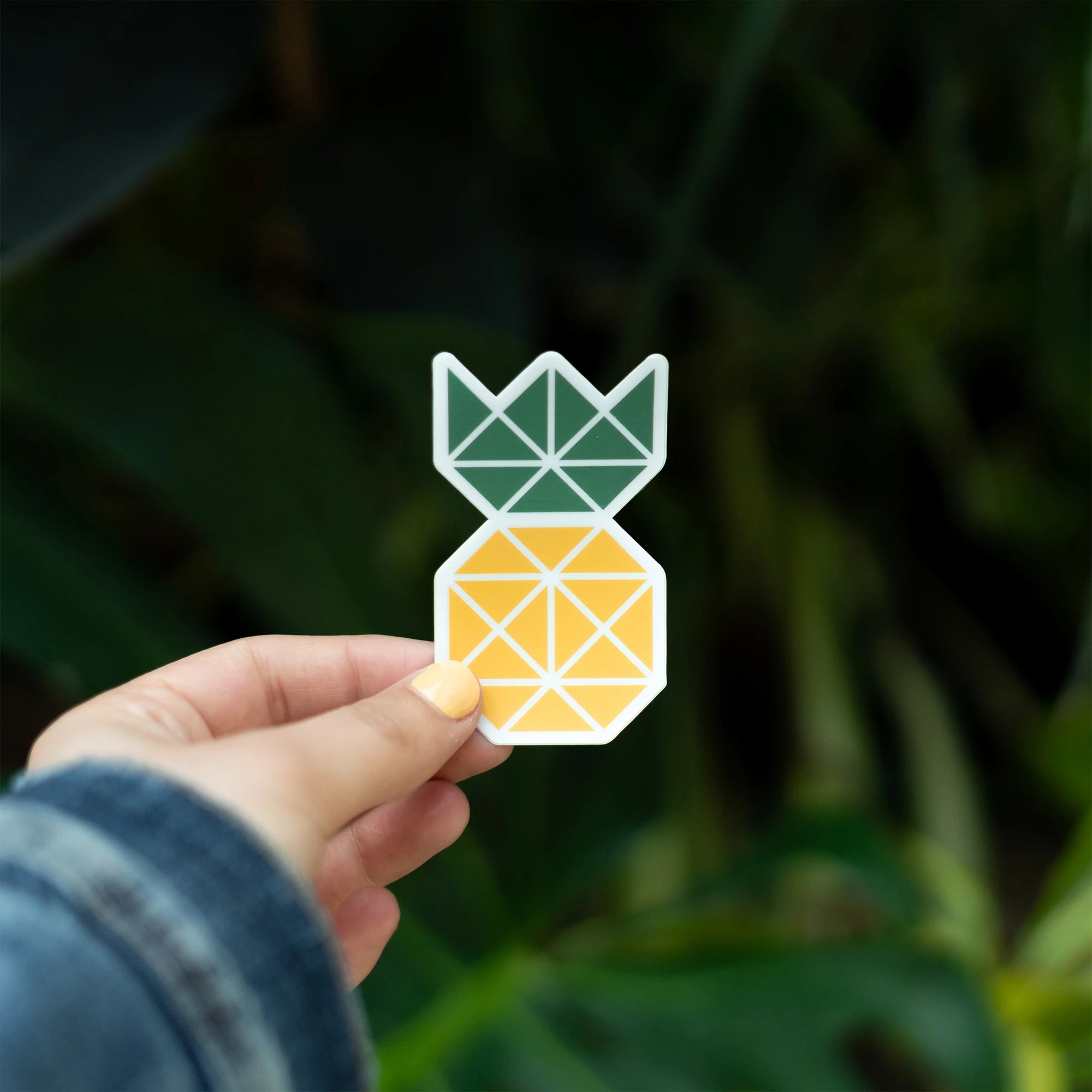 Custom die-cut pineapple sticker held by a person, featuring geometric design in green and yellow against a nature backdrop.
