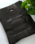 Custom die cut handle bags in black featuring 'Amare' logo, ideal for brand promotions and stylish packaging.