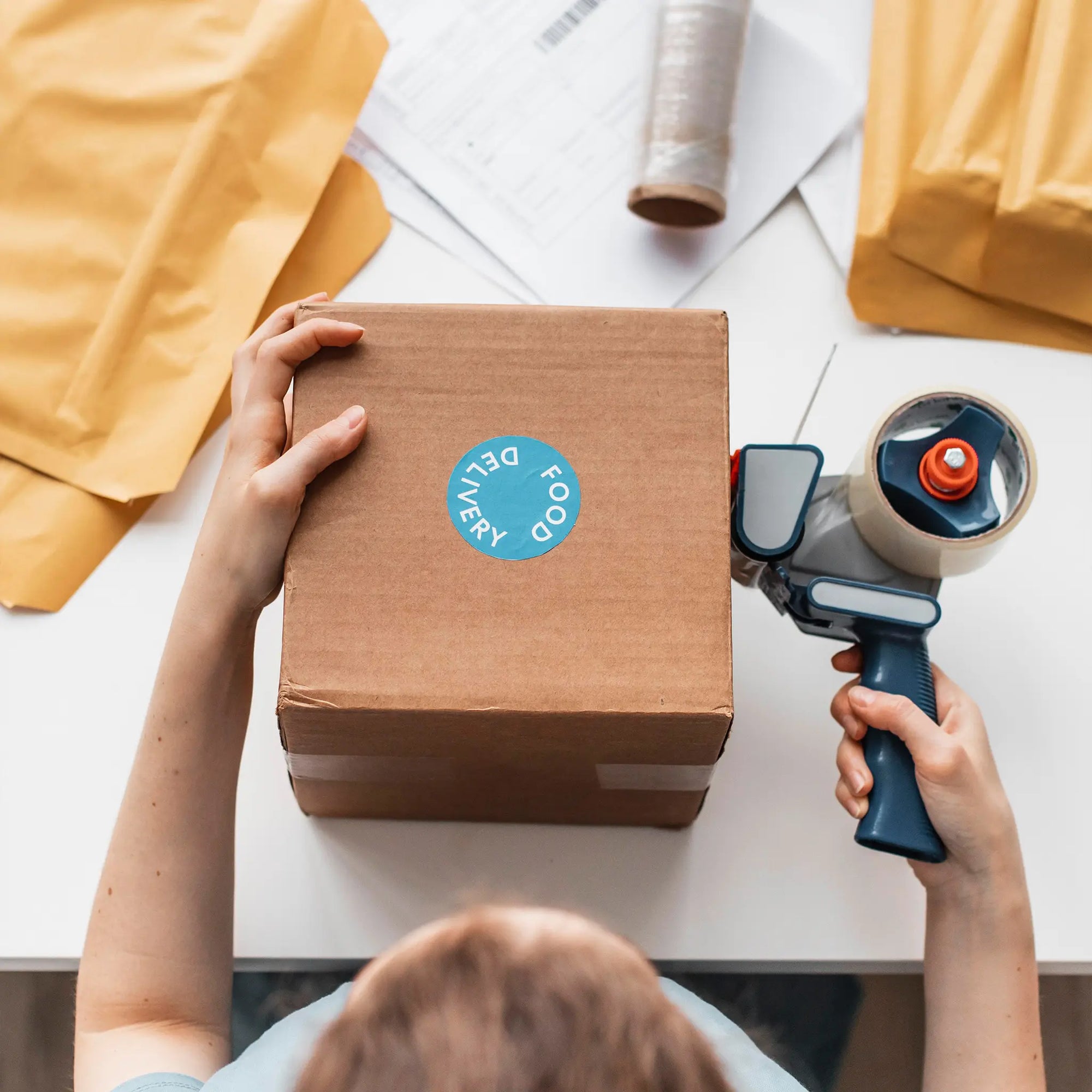 Person applying a custom round sticker to a cardboard box for branding and delivery.
