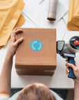 Person applying a custom round sticker to a cardboard box for branding and delivery.