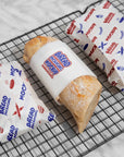 Three pieces of custom deli paper wrapped around fresh bread on a cooling rack, showcasing vibrant designs and branding.