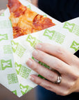 Custom deli paper featuring vibrant branding, holding a slice of pizza. Ideal for restaurants and food services.