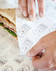 Custom deli paper being used to wrap a sandwich, showcasing FSC and FDA certified food-safe ink.