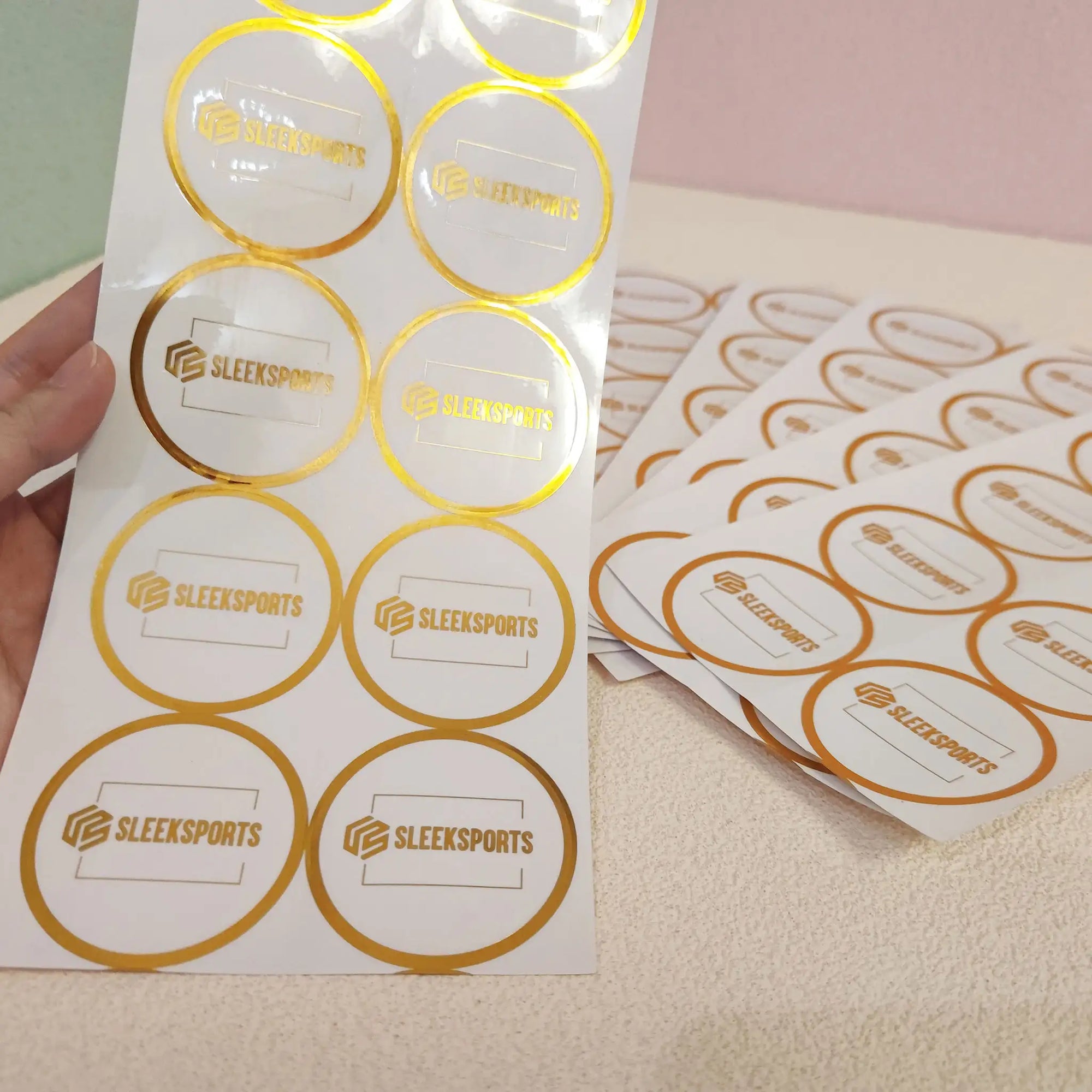 Custom round stickers with gold foil for SleekSports branding on a textured surface.