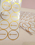 Custom round stickers with gold foil for SleekSports branding on a textured surface.