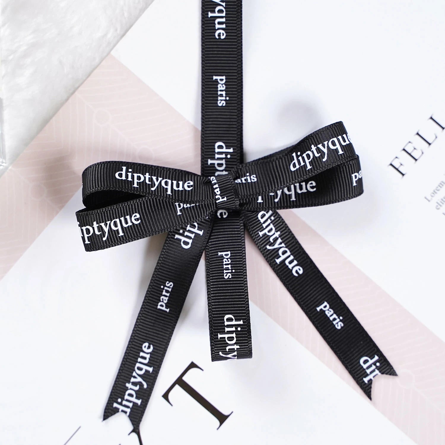 Custom black grosgrain ribbon with "diptyque" and "paris" text, elegantly tied around a gift package.