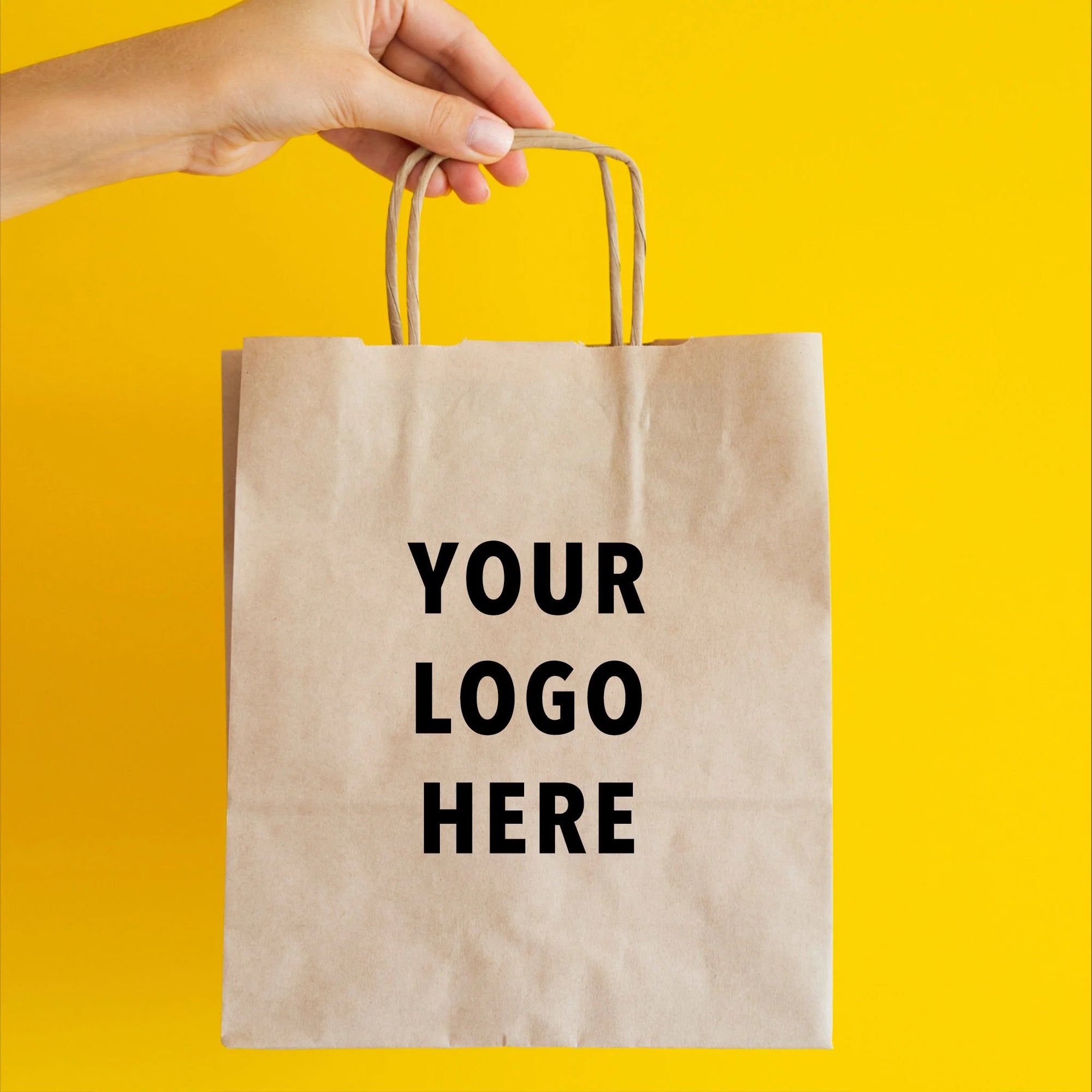 A hand holding a custom paper bag with blank logo space against a bright yellow background.