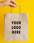 A hand holding a custom paper bag with blank logo space against a bright yellow background.