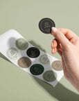 Hand holding a custom round sticker from a sheet on a green background, showcasing branding and design options.