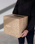Person holding a custom shipping box with playful designs and branding, showcasing premium packaging.
