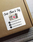 Custom square sticker on a package with social media handles and a camera graphic, inviting customers to engage.