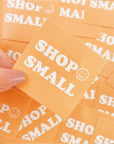 Custom orange square sticker displaying "SHOP SMALL" with a smiling face, emphasizing support for local businesses.