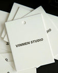 Custom hang tags featuring a minimalist design with 'VINMEN STUDIO' printed in bold black on a white background.