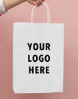 Custom white paper bag held by hand, featuring placeholder text for branding with 'YOUR LOGO HERE'.