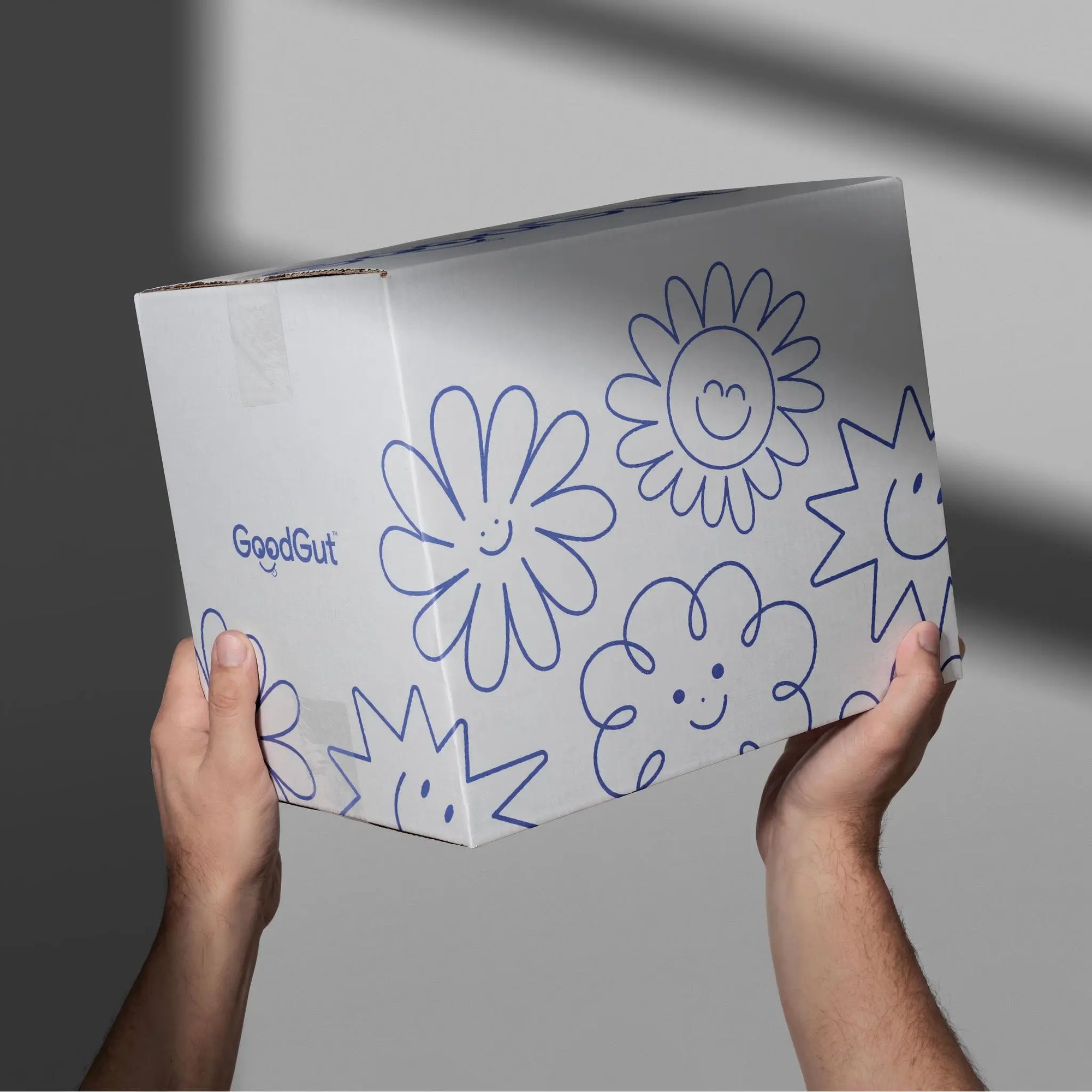 Custom shipping box with cheerful flower designs, held by hands, showcasing unique brand packaging.