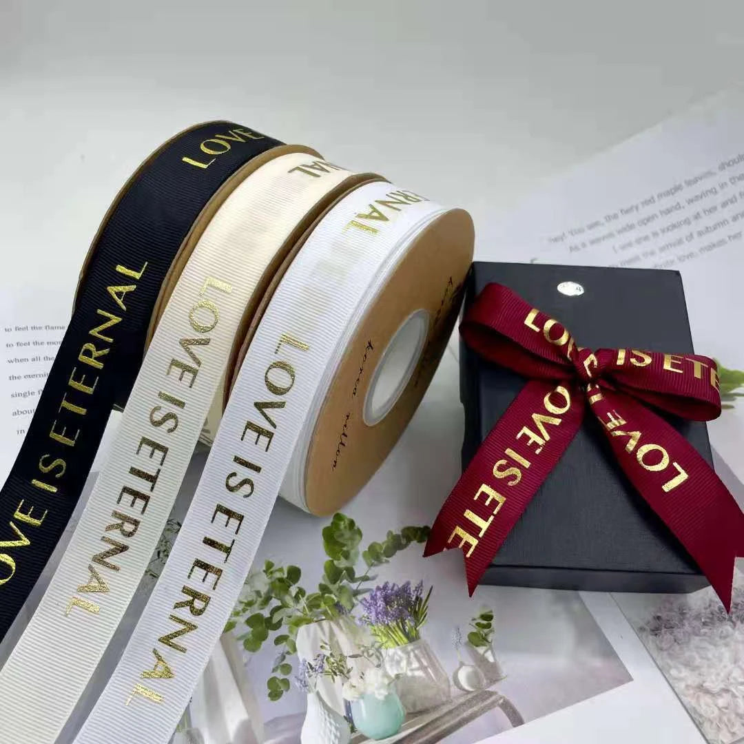 Custom grosgrain ribbon rolls in black, white, and red with "LOVE IS ETERNAL" text, perfect for packaging and crafts.
