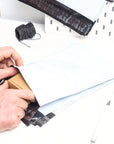 Hands sealing a package in a wholesale poly mailer with shipping supplies on a desk.