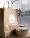 Eco-friendly custom paper bag with 'Fresh Craving' logo next to food containers on a wooden table.
