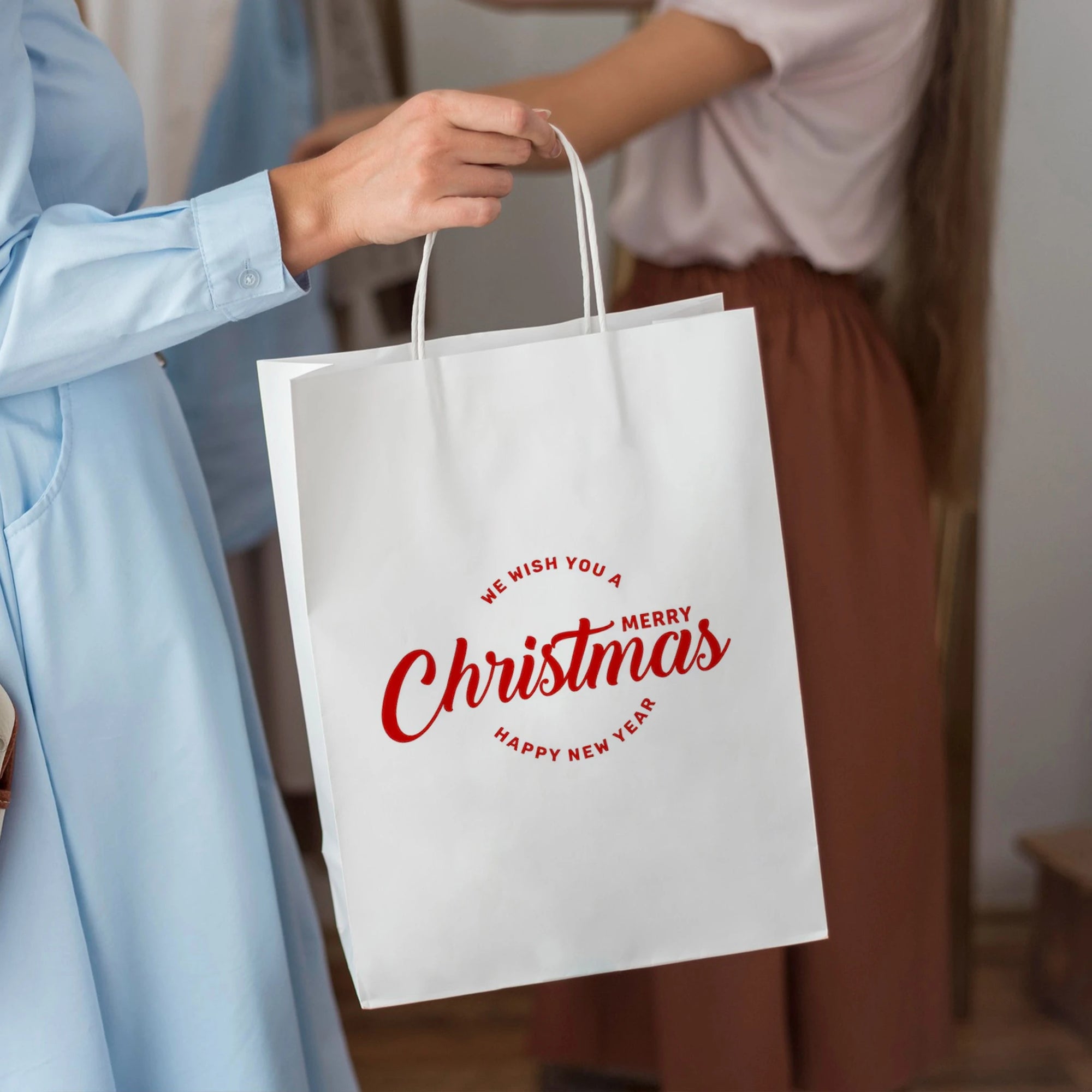 Woman holding a custom white paper bag with a Christmas greeting design for holiday gifting.