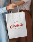 Woman holding a custom white paper bag with a Christmas greeting design for holiday gifting.