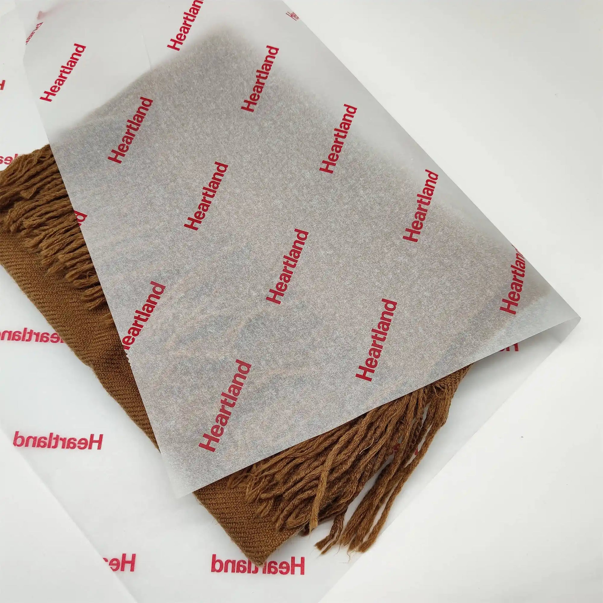 Custom tissue paper featuring brand name "Heartland" wrapping a brown scarf for elegant packaging.