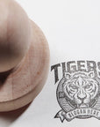 Custom rubber stamp imprints a tiger logo with the text "TIGERS" and "SLOGAN HERE" on paper.