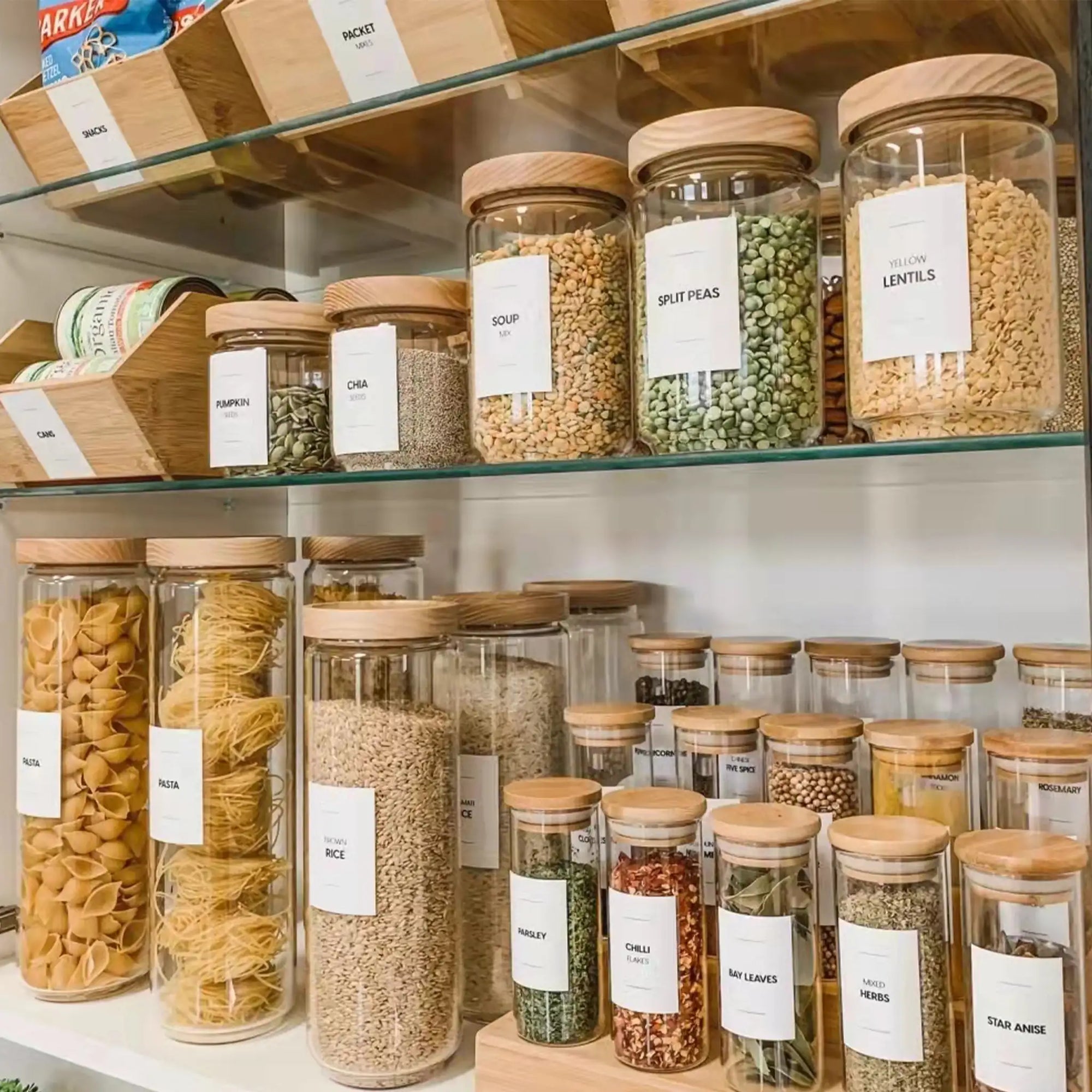 Organized pantry shelves with clear jars and labels for grains, pastas, and beans, featuring wooden lids for a stylish look.