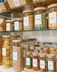 Organized pantry shelves with clear jars and labels for grains, pastas, and beans, featuring wooden lids for a stylish look.