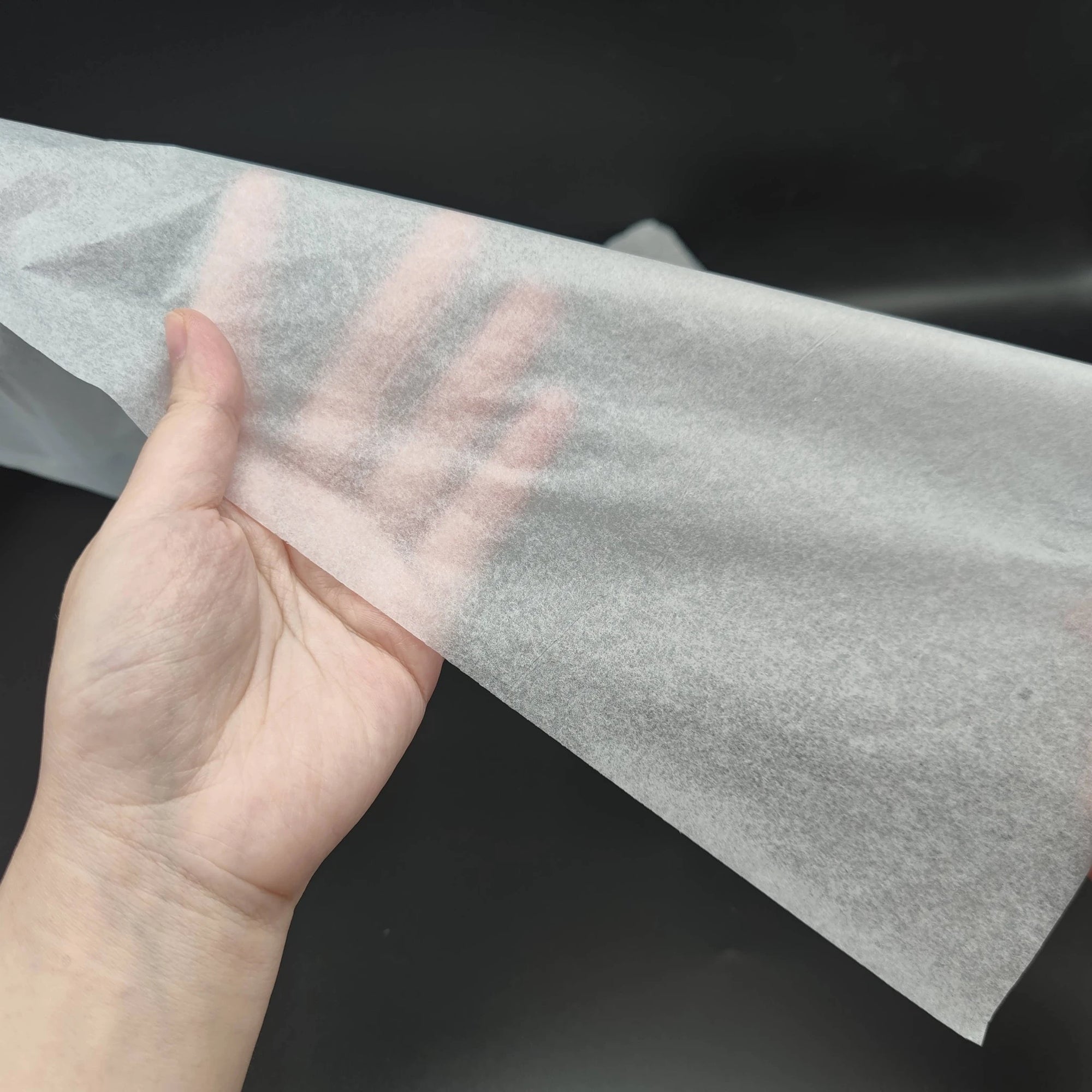 Hand holding a high-quality, eco-friendly tissue paper sheet against a dark background.