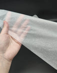 Hand holding a high-quality, eco-friendly tissue paper sheet against a dark background.