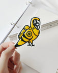 Custom die-cut yellow parrot sticker held above a notebook on a white background.