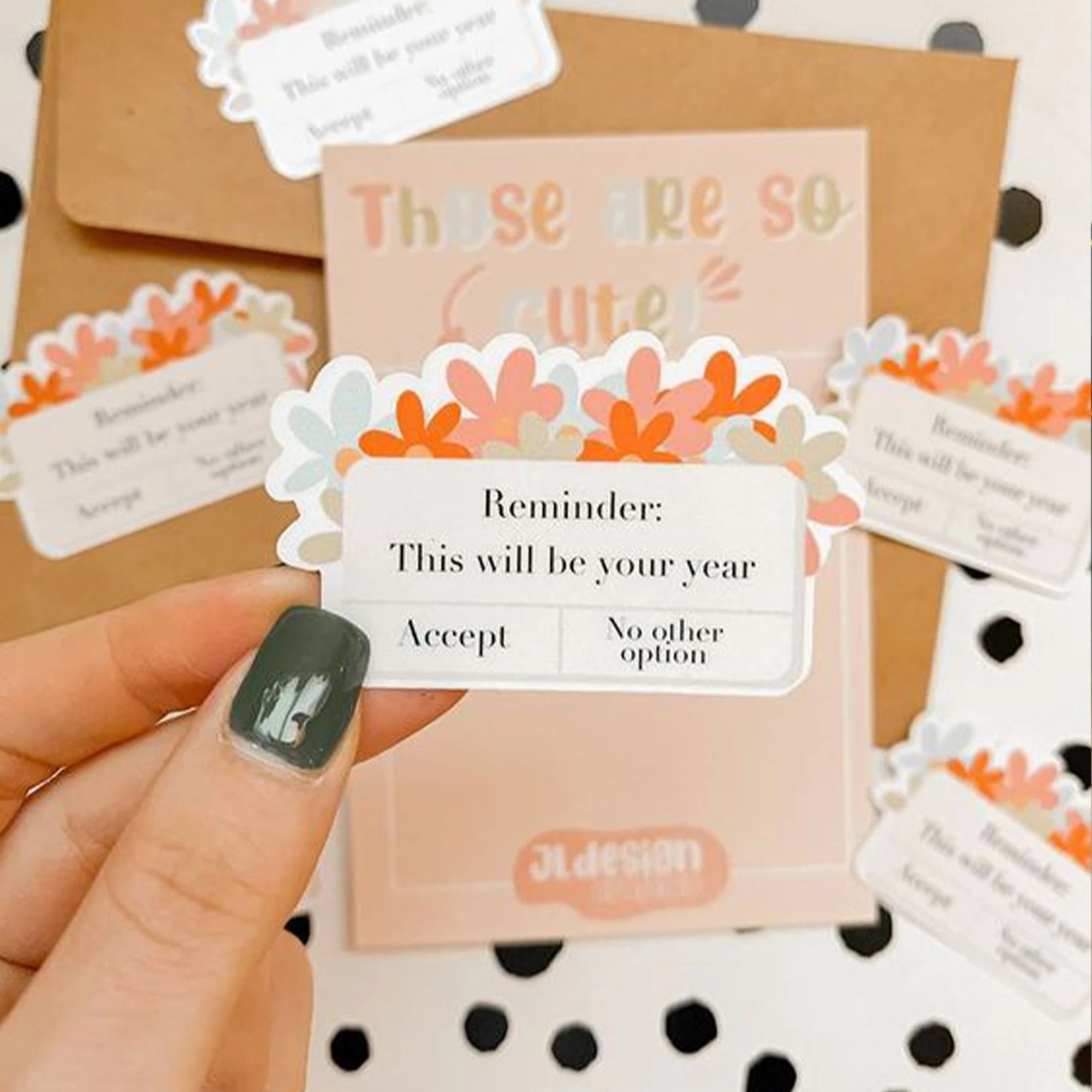 Custom die-cut stickers with floral designs and motivational messages held by a person with green nail polish.
