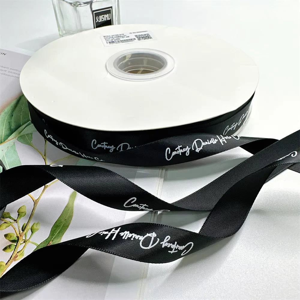 Custom satin ribbon on a spool, featuring elegant black color and personalized design for gift wrapping and events.