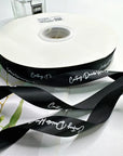 Custom satin ribbon on a spool, featuring elegant black color and personalized design for gift wrapping and events.