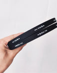 Hand holding two black custom cotton ribbons with printed text for personalized branding.