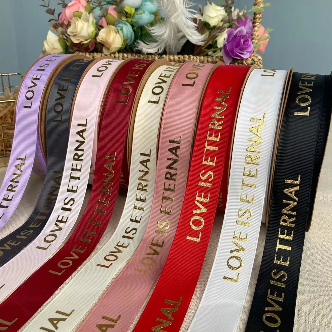 Custom grosgrain ribbons in various colors with "Love is Eternal" printed in gold, perfect for events and projects.