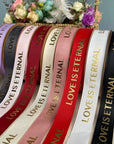 Custom grosgrain ribbons in various colors with "Love is Eternal" printed in gold, perfect for events and projects.