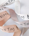 Custom herringbone ribbon in pink and white with playful 'Kitty N Tug' text, perfect for packaging and crafts.