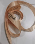 Custom satin ribbon in soft peach color with logo of Cellesis Clinic, elegantly coiled on a white surface.