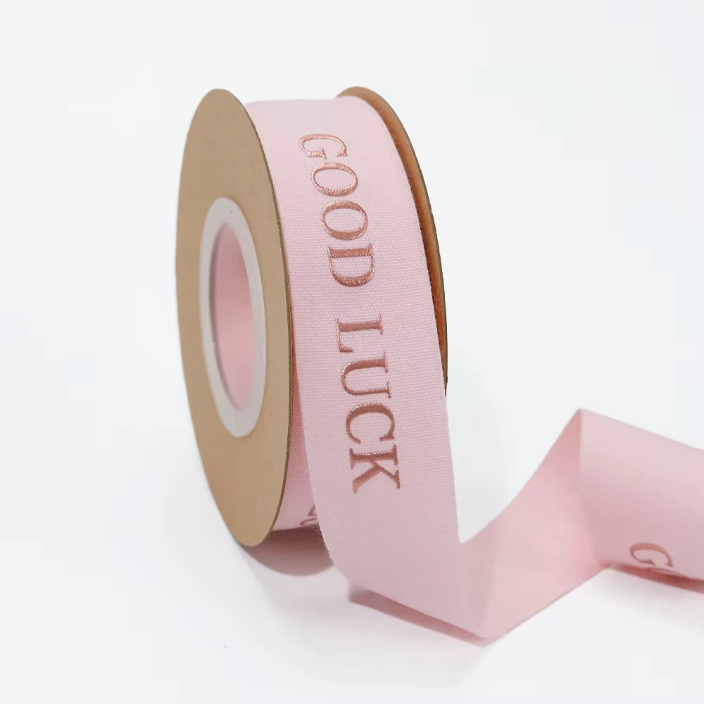 Custom cotton ribbon in soft pink with "GOOD LUCK" text, perfect for gifts and special events.