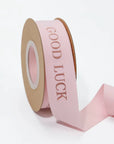 Custom cotton ribbon in soft pink with "GOOD LUCK" text, perfect for gifts and special events.