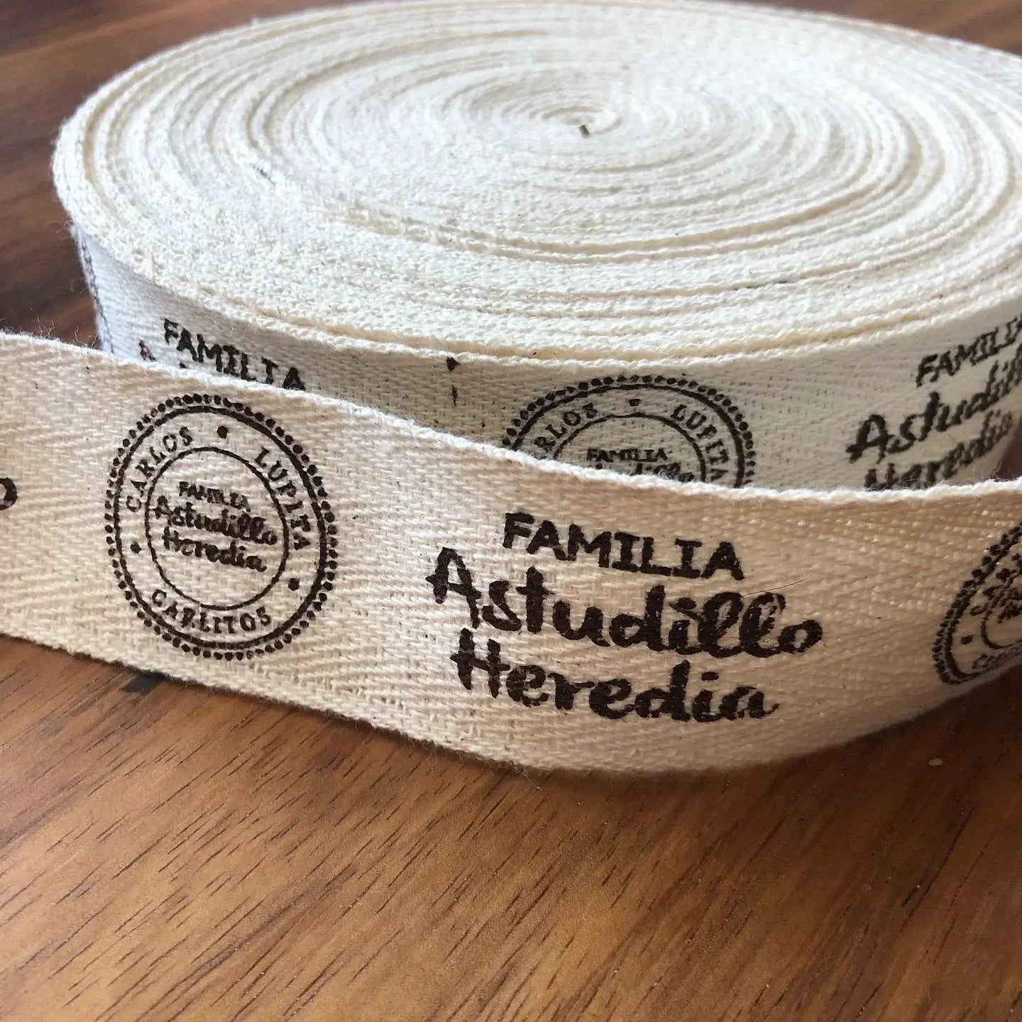 Custom cotton ribbon featuring the printed text 'Familia Astudillo Heredia,' laid on a wooden surface.