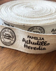 Custom cotton ribbon featuring the printed text 'Familia Astudillo Heredia,' laid on a wooden surface.