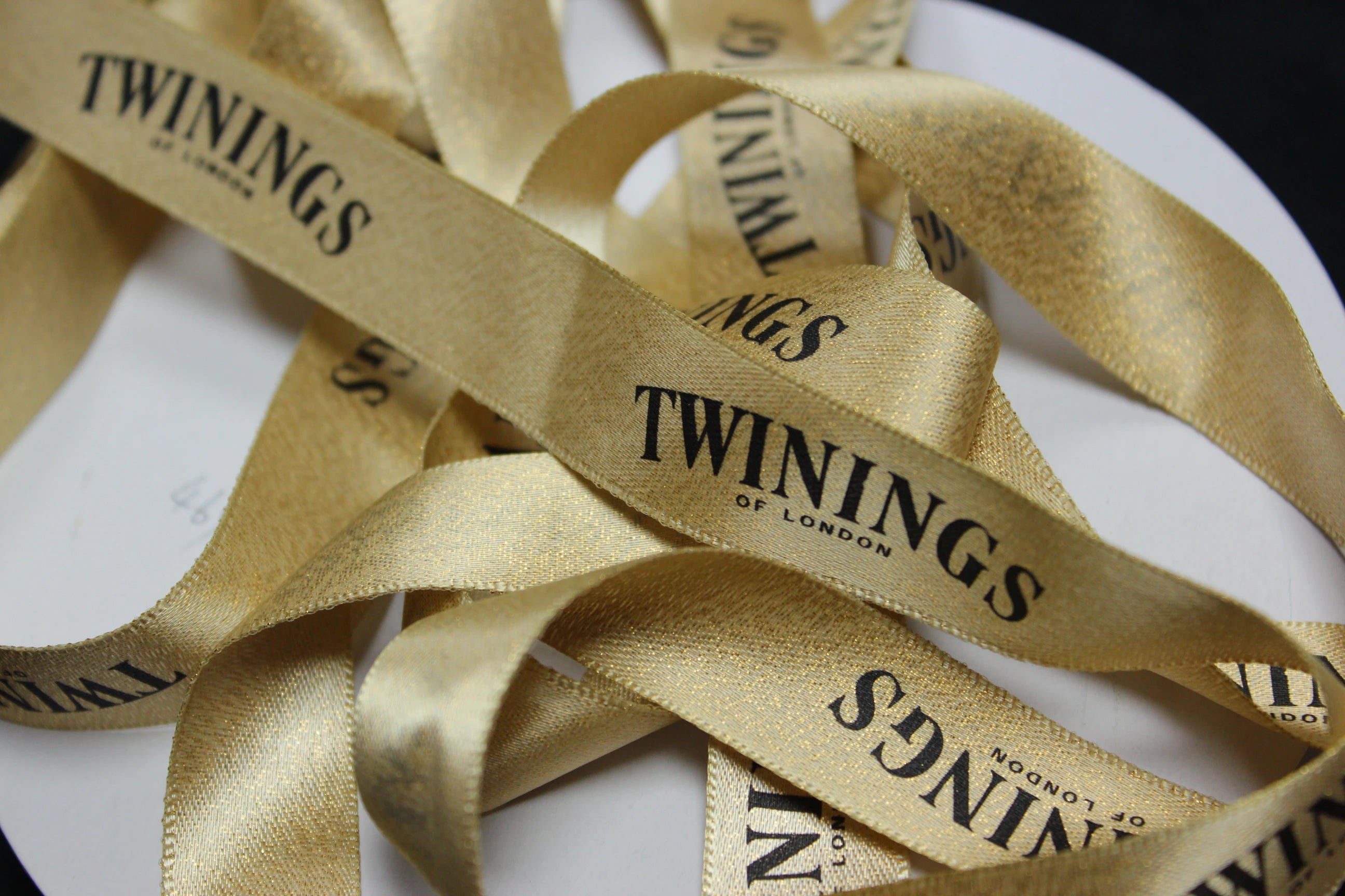 Gold metallic ribbon with "Twinings of London" printed, showcasing shimmer and elegance for packaging or décor.