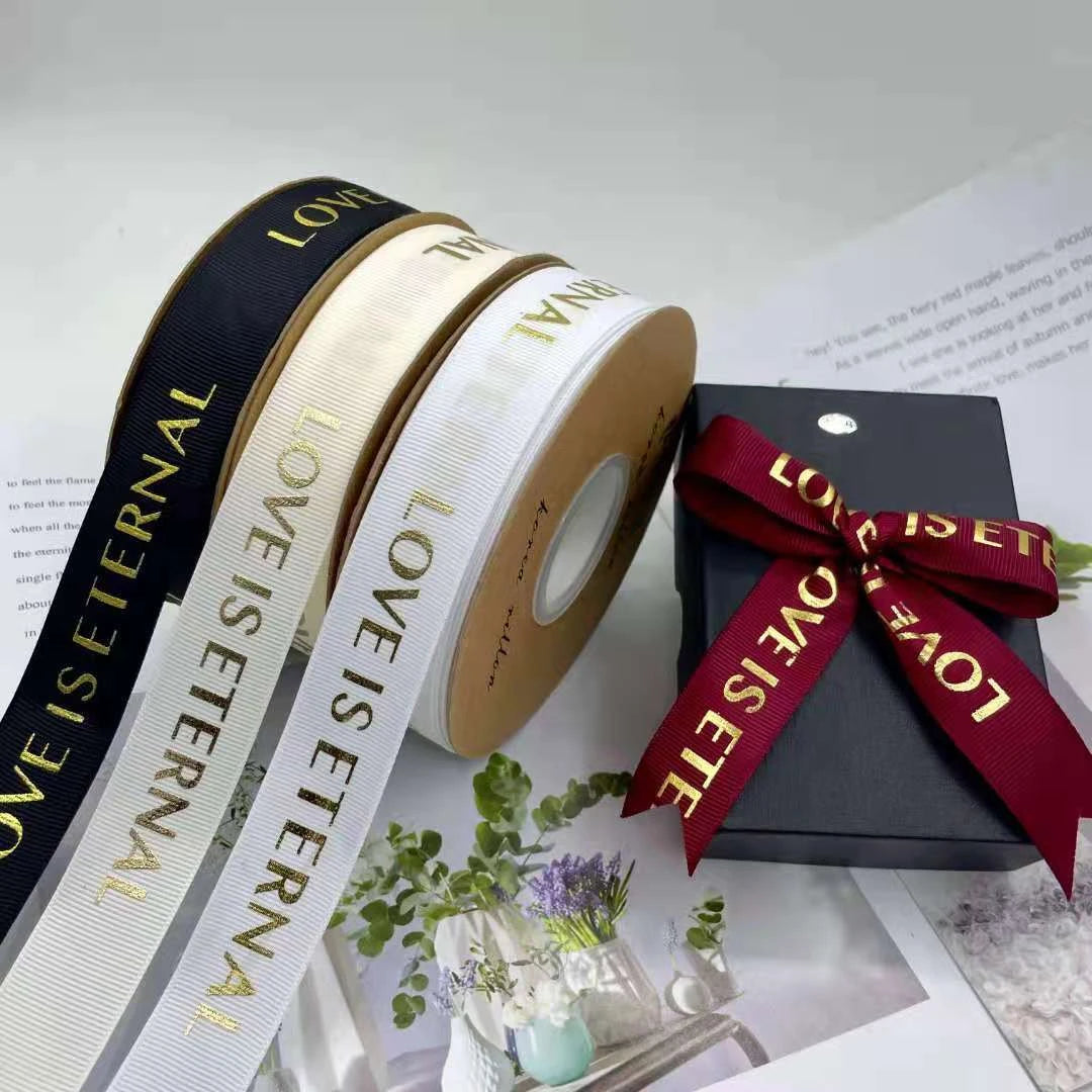 Custom grosgrain ribbon rolls in black, white, and red with &quot;LOVE IS ETERNAL&quot; text, perfect for packaging and crafts.