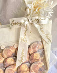 Custom satin ribbon with "love you" text decorates a stylish handbag next to luxury cookies and a flower.